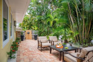 A patio with brick flooring, two beige chairs, a table with a bottle and glasses, and a row of red flowers along the wall. - The Palm at Bean Point - Luxury Coastal Retreat with Heated Pool, Walk to Beach (Anna Maria)