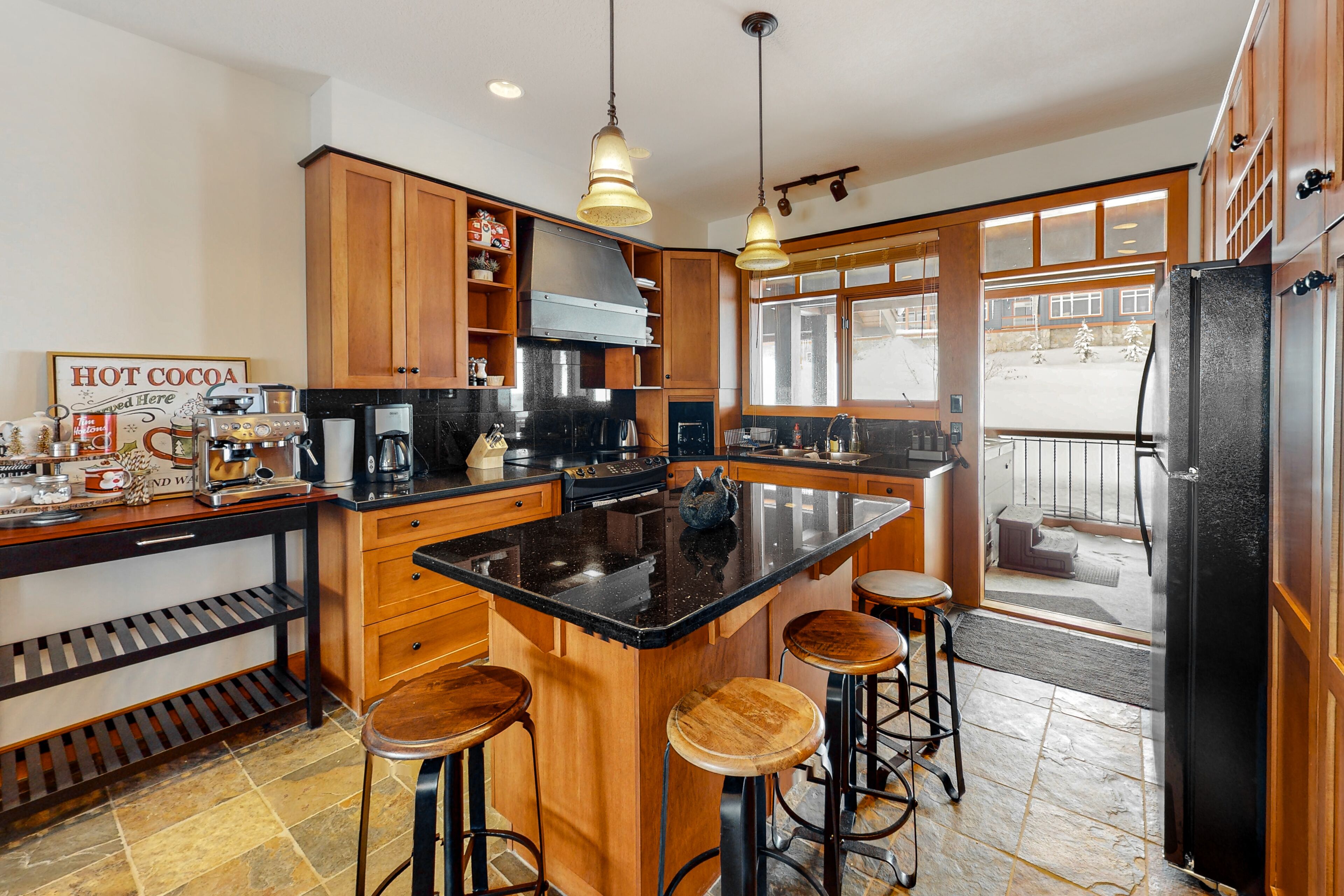 A kitchen with wooden cabinets, a black countertop, and a central island with stools.