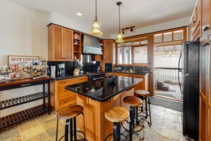 A kitchen with wooden cabinets, a black countertop, and a central island with stools. - Blacksmith Lodge by Okanagan Premier (Beaverdell)