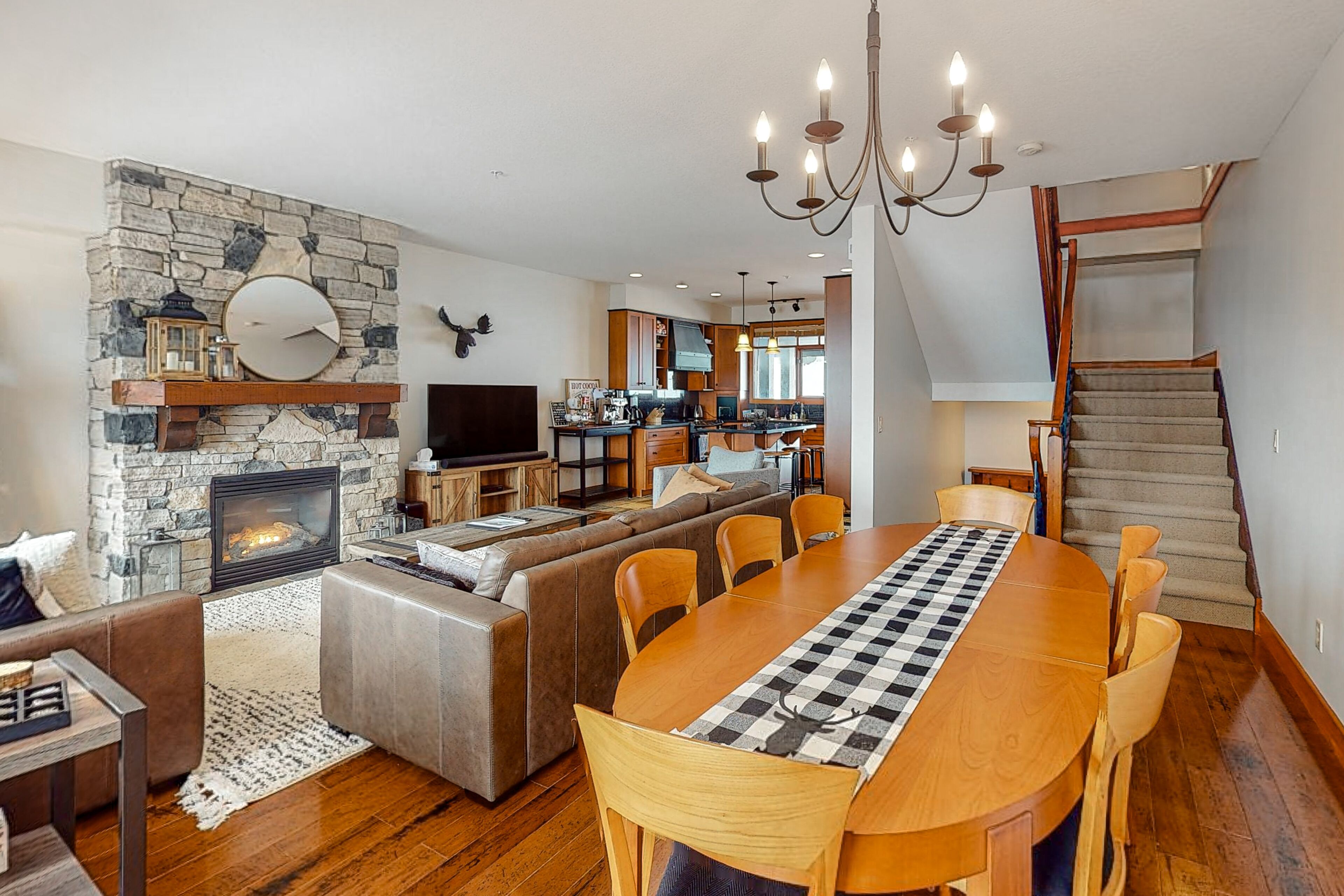 A spacious living area with a stone fireplace, a large dining table, and a kitchen in the background.