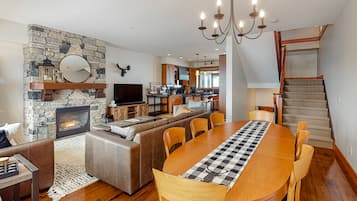 A spacious living area with a stone fireplace, a large dining table, and a kitchen in the background.