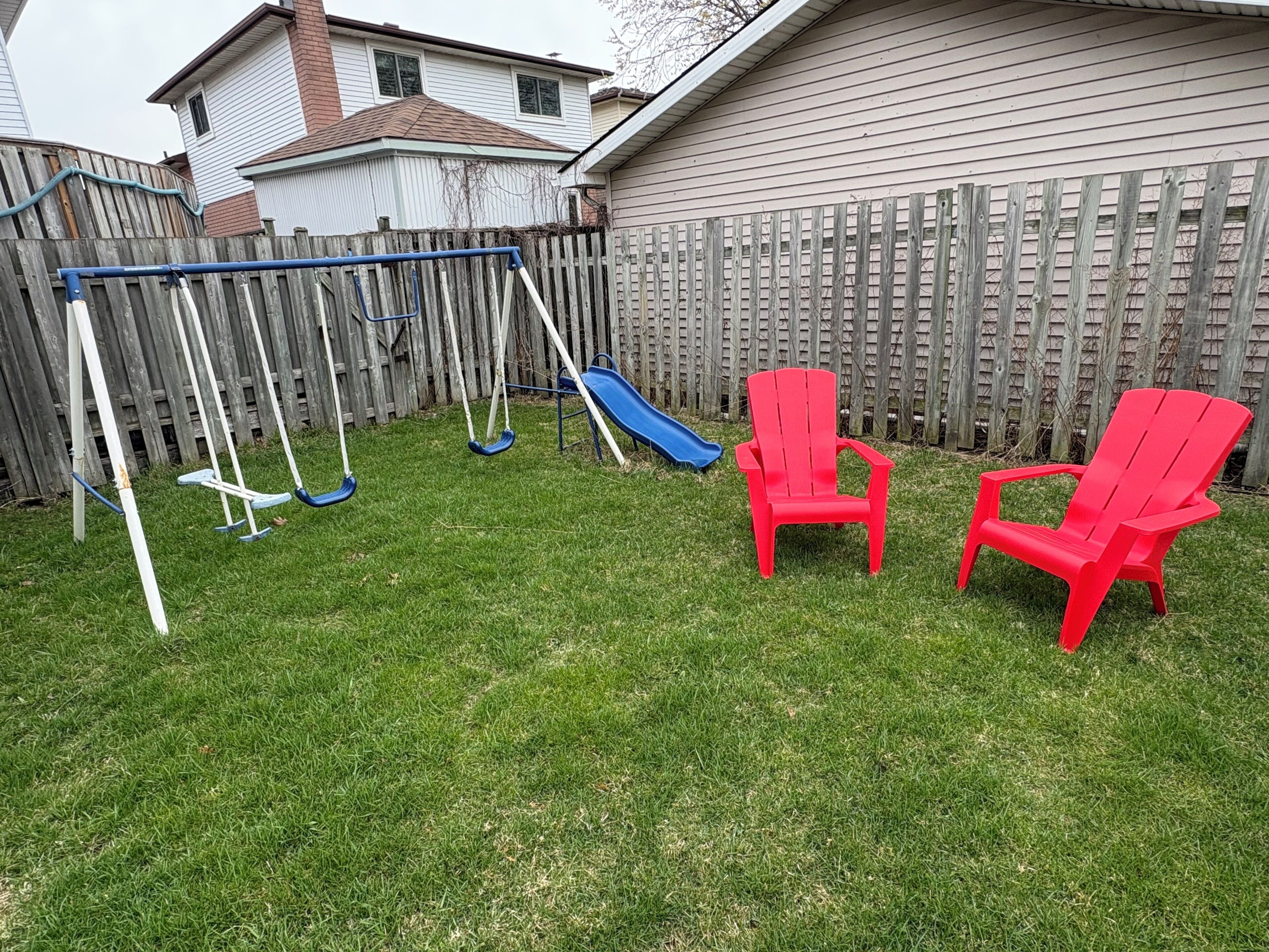 Un jardin avec une balançoire, deux chaises rouges et un toboggan bleu.