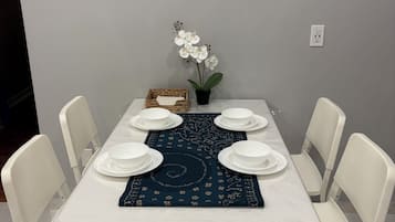 Ruokapöytä valkoisine tuoleineen, koristeellinen taideteos seinällä pöydän yläpuolella ja ruukussa oleva orkidea.