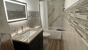 Une salle de bain moderne équipée d’un meuble-lavabo, d’un évier, d’un miroir, de toilettes et d’une douche.