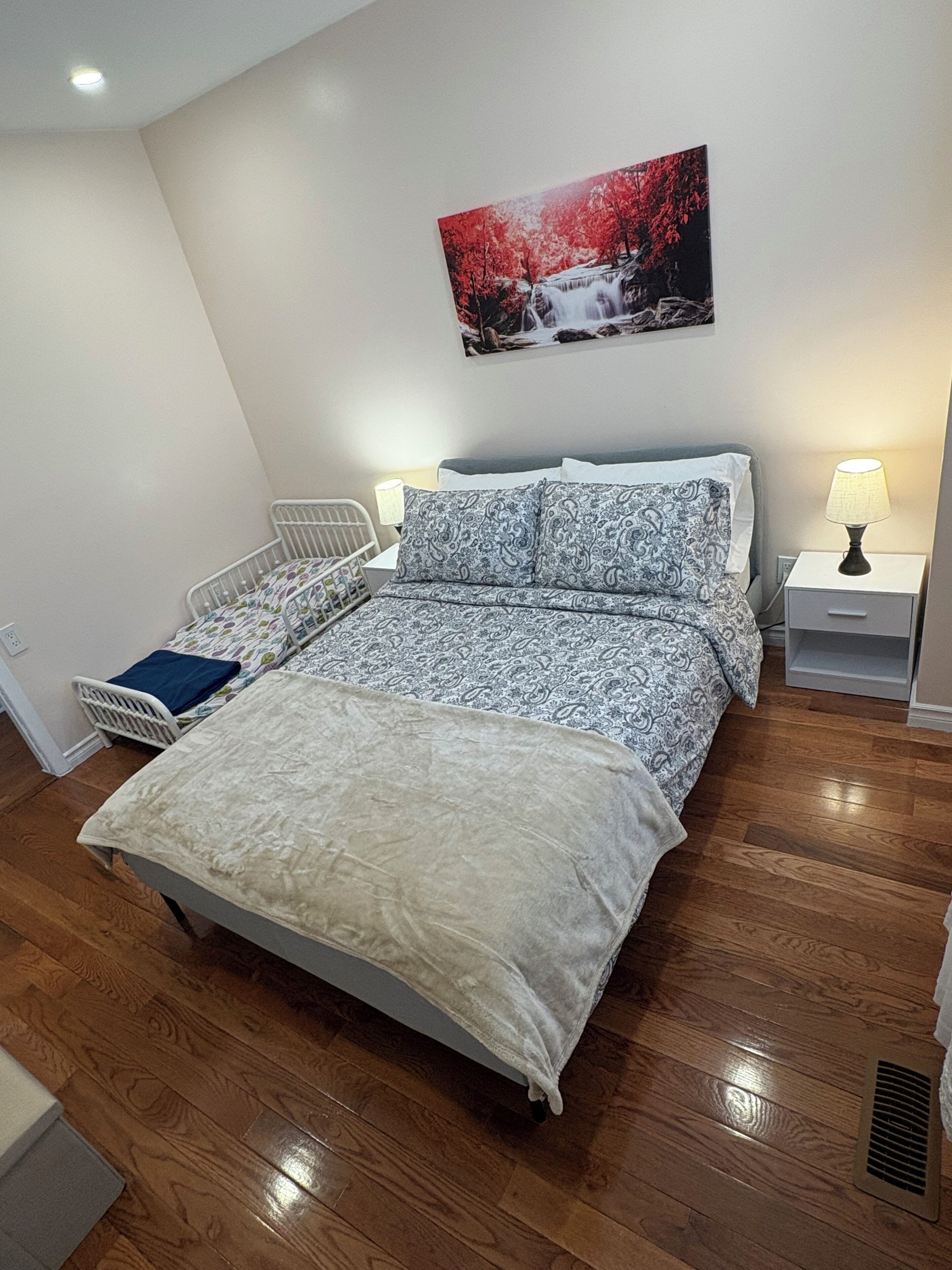 A bedroom with a bed, bedside tables, a nightstand, a wall-mounted picture, and a radiator.