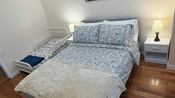 A bedroom with a bed, bedside tables, a nightstand, a wall-mounted picture, and a radiator.
