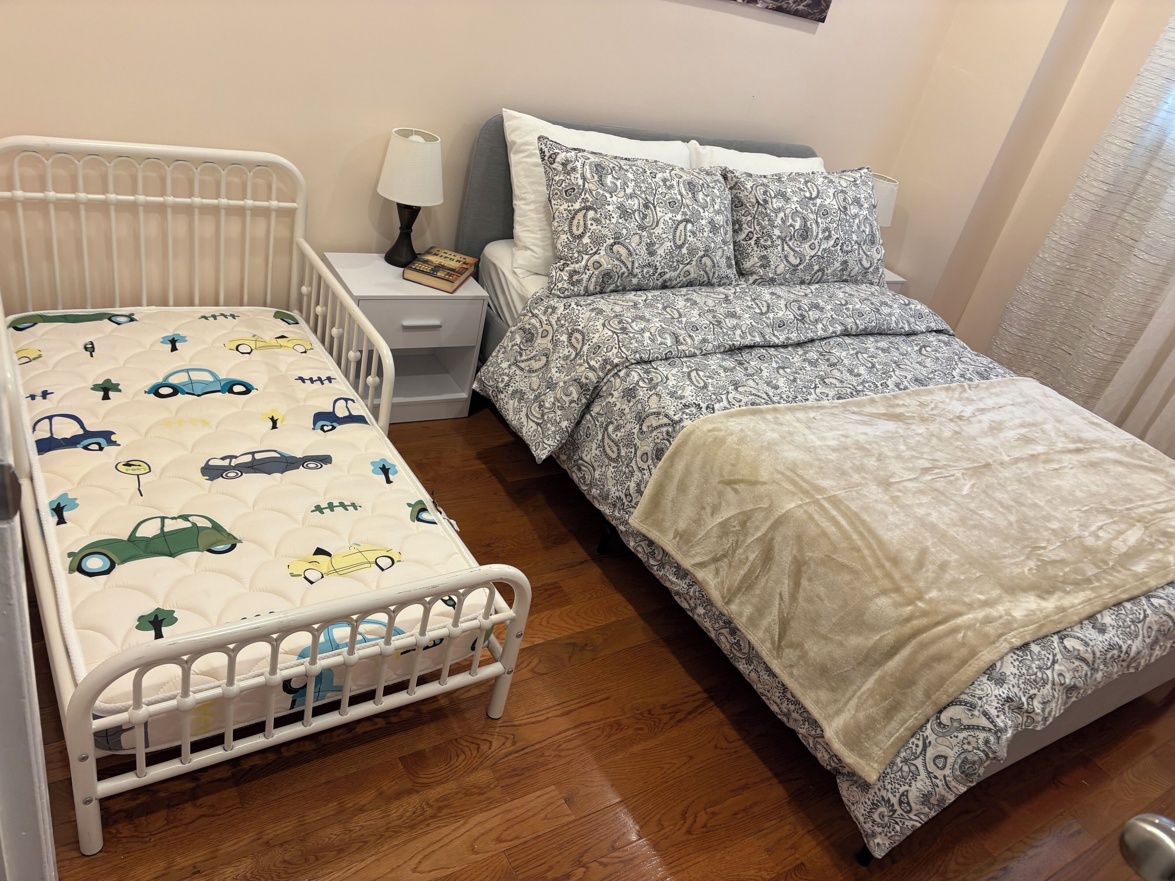 Un lettino per bambini con materasso a tema automobilistico, un comodino con una lampada e una coperta a motivi decorativi.