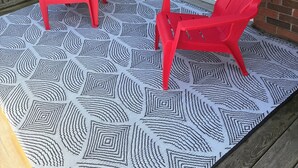 A patio with two red chairs and a patterned rug.