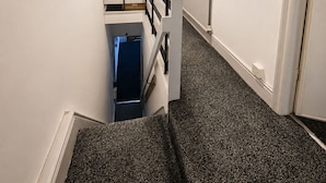 A narrow hallway with a staircase, a radiator, and a door leading to another room. - Skip for now (Manchester)
