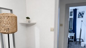 A room with a chair, a hanging lamp, a small shelf with a plant, and a doorway leading to another room. - Skip for now (Manchester)