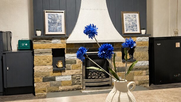 A kitchen with a clock, a fireplace, and a vase with flowers. - Skip for now (Manchester)
