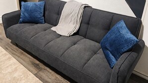 A grey sofa with two blue pillows, a white throw blanket, and a wooden floor. - Skip for now (Manchester)