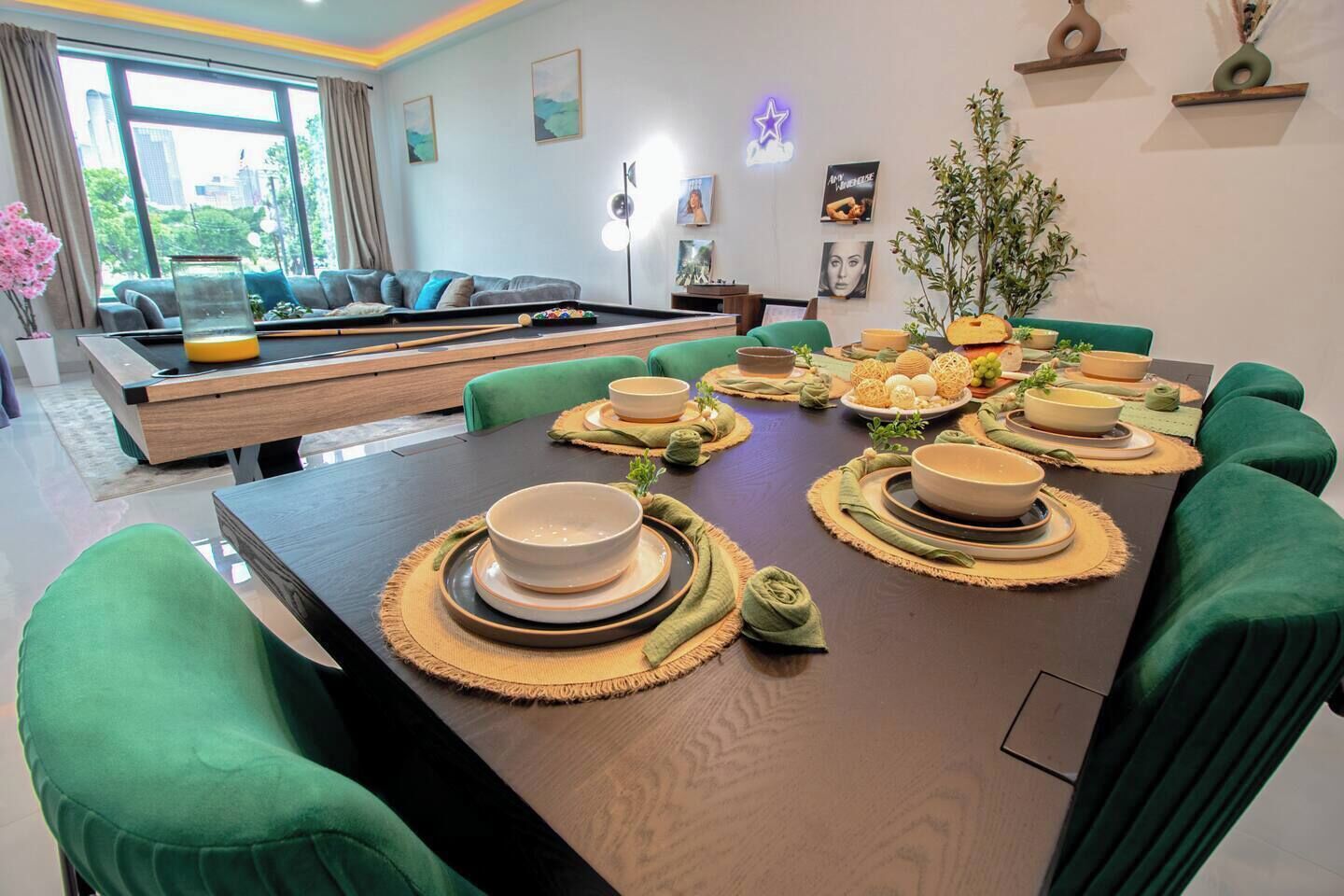 A dining area with a long table set for a meal, green upholstered chairs, and a sofa in the background.