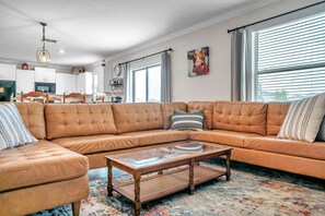 Ein Wohnzimmer mit einem großen, L-förmigen Ecksofa, einem Glastisch und einem Teppich mit Muster.