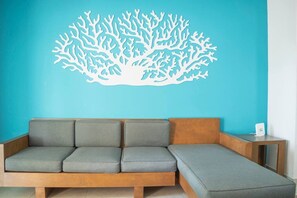 Ein modernes Sofa mit Holzrahmen und grauen Kissen vor einer türkisblauen Wand.