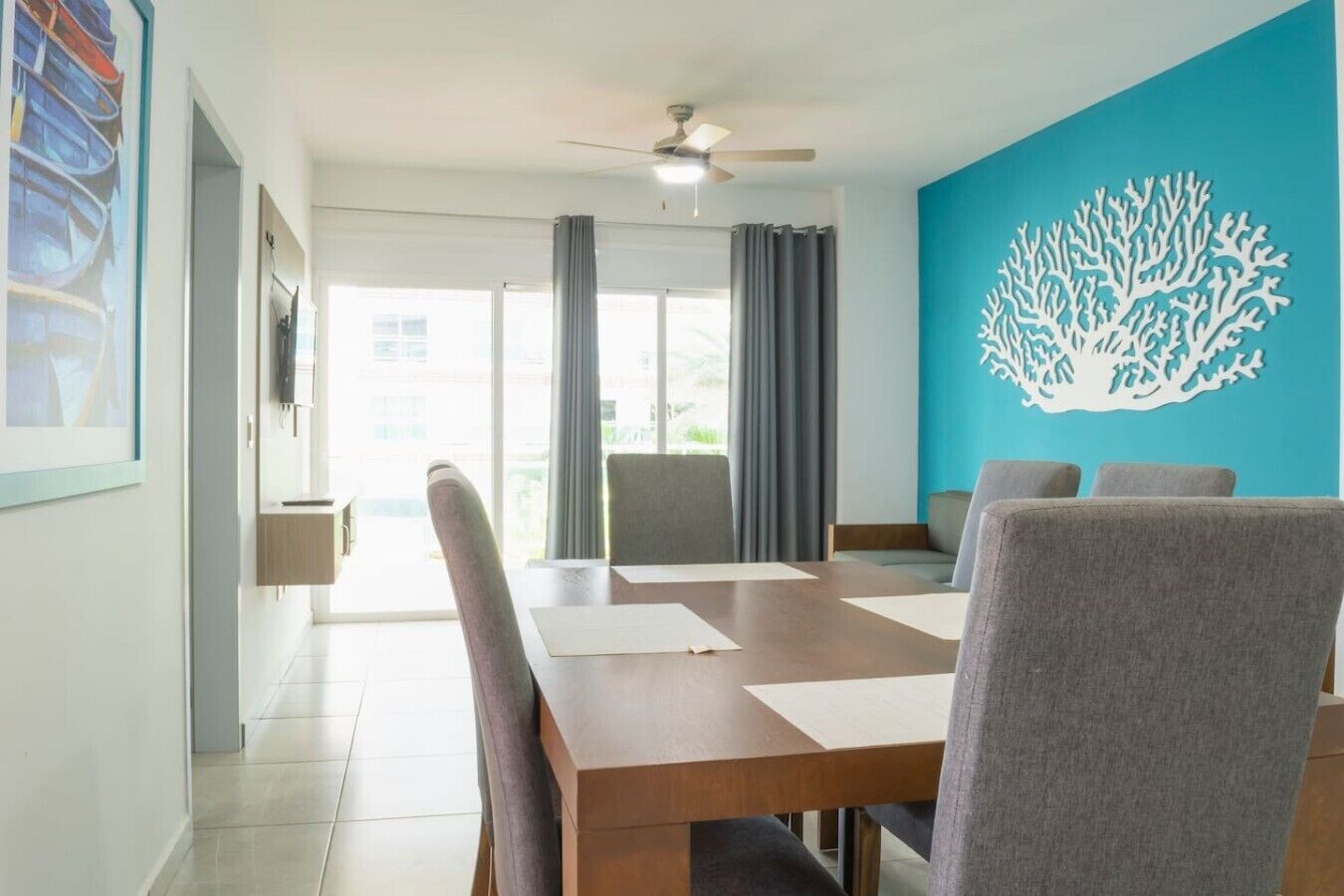 A dining area with a table, chairs, a ceiling fan, and a large window with curtains.