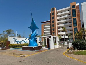 A hotel entrance with a large blue sculpture, a sign reading 'Pacifica,' and a multi-story building with balconies. - Depa con alberca infinity frente a la marina (Mazatlán)