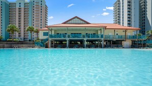 Um hotel com piscina, área coberta com cadeiras e edifícios altos ao fundo.
