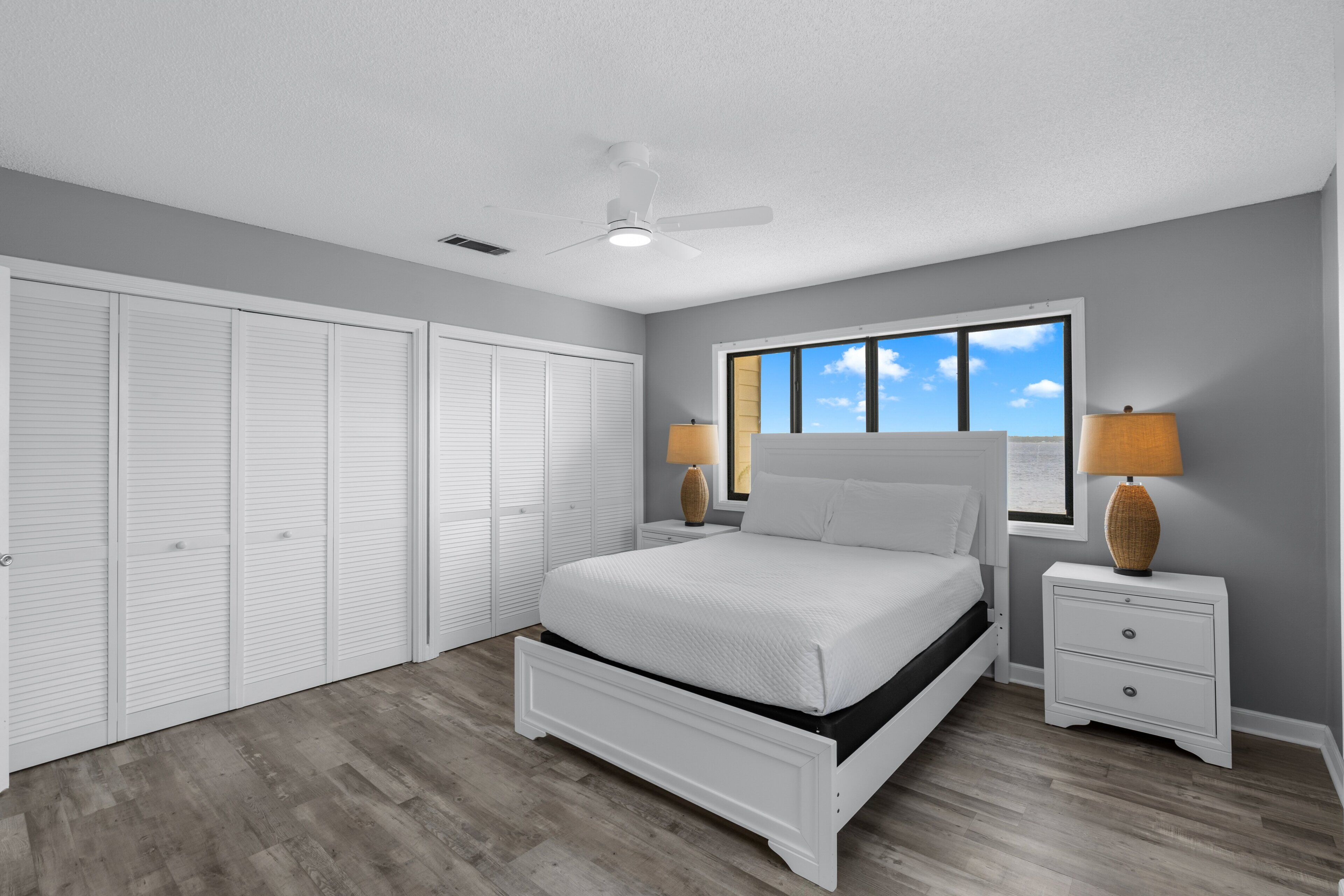A bedroom with a bed, nightstands, a ceiling fan, a window with a view, and a closet.