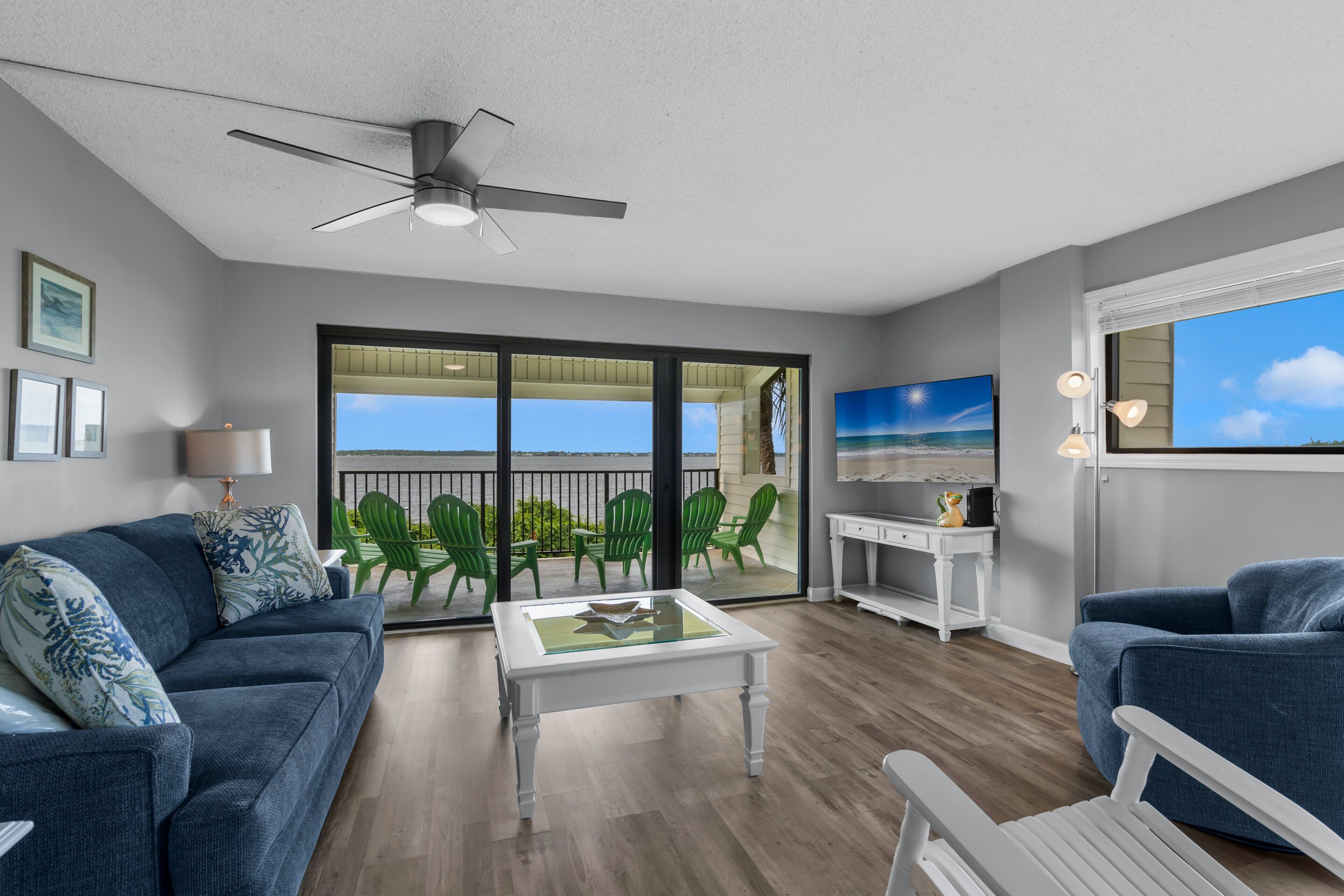 A spacious living room with a balcony, a ceiling fan, and a view of the sea.