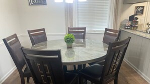A round glass dining table with six dark wooden chairs, a small potted plant, and a welcome sign on the wall. - Day Dreams Begin at Bryant Denny Stadium 6 ppl (Tuscaloosa)