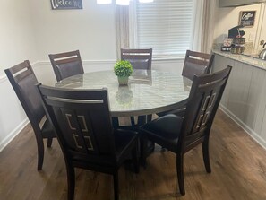 A round glass dining table with six dark wooden chairs, a small potted plant, and a welcome sign on the wall. - Day Dreams Begin at Bryant Denny Stadium 6 ppl (Tuscaloosa)
