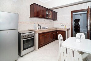 Een keuken met een koelkast, oven, houten kastjes, een aanrecht en een eettafel met stoelen.