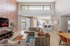 A modern living room with a sectional sofa, a coffee table, and a TV on a wall with a patterned wallpaper. - Lyra - Dual Retreat - In Old Town Scottsdale (Scottsdale)