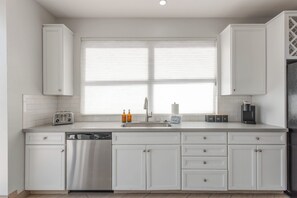 A modern kitchen with white cabinetry, a built-in dishwasher, a toaster, and a coffee machine. - Lyra - Dual Retreat - In Old Town Scottsdale (Scottsdale)