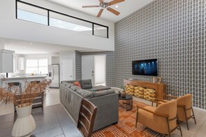 A spacious living area with a grey sectional sofa, a wooden coffee table, and a TV mounted on a patterned wall. - Lyra - Dual Retreat - In Old Town Scottsdale (Scottsdale)