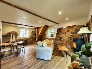 A rustic interior with a stone wall, wooden floor, a sofa, a table, and a staircase.
