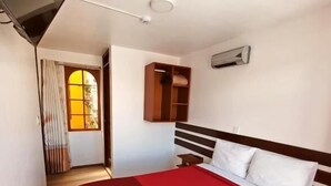A hotel room with a bed, a TV, a wooden floor, a window with curtains, and a door leading to another room. - PUKANTU  (Puno)
