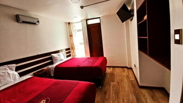 A hotel room with two beds, a flat-screen TV, a ceiling fan, and a wooden floor. - PUKANTU  (Puno)
