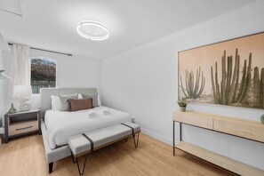 Ein modernes Schlafzimmer mit Bett, Nachttischen, einer Bank, einem Fenster und einem Bild einer Sukkulente.
