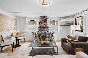 Ein Wohnzimmer mit Kamin aus Stein, einem Esstisch und einer Couch.