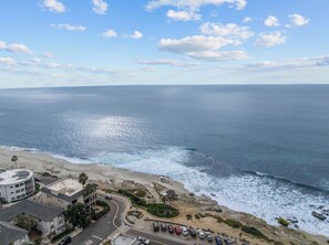 Blick auf die Küste mit Strand, Meer und Gebäuden, darunter ein Parkplatz.