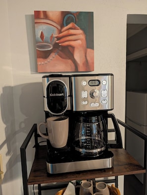 Eine Cuisinart-Kaffeemaschine auf einer schwarzen und silbernen Standfläche, neben ihr eine weiße Tasse.