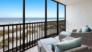 Un balcon donnant sur la plage, des meubles en osier et une rambarde en métal noir.