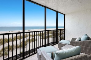 Ein Balkon mit Blick auf den Strand, Korbmöbel und ein schwarzes Metallgeländer.