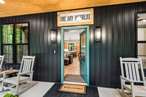 Een houten deur met een bord waarop 'THE DAY RETREAT' staat en een welkomstmat.