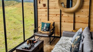 Una habitación con ventanas amplias, una pared de madera, un sofá, una silla y una pequeña mesa.