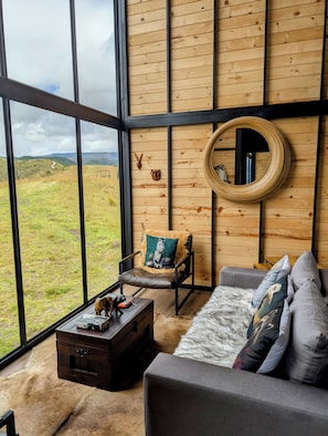 Una habitación con ventanas amplias, una pared de madera, un sofá, una silla y una pequeña mesa.