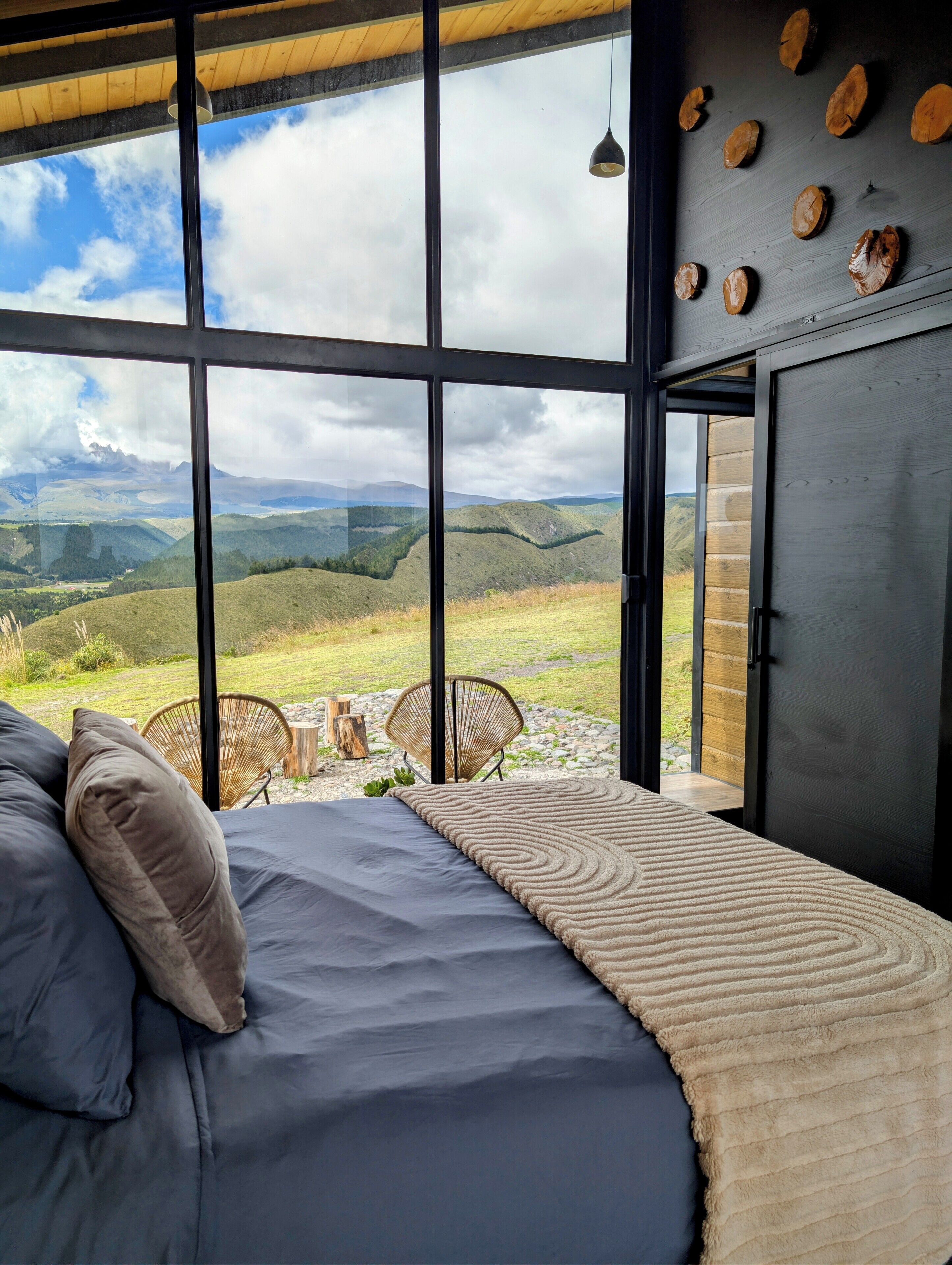 A bedroom with a large window, a bed, a chair, and a view of a mountainous landscape.