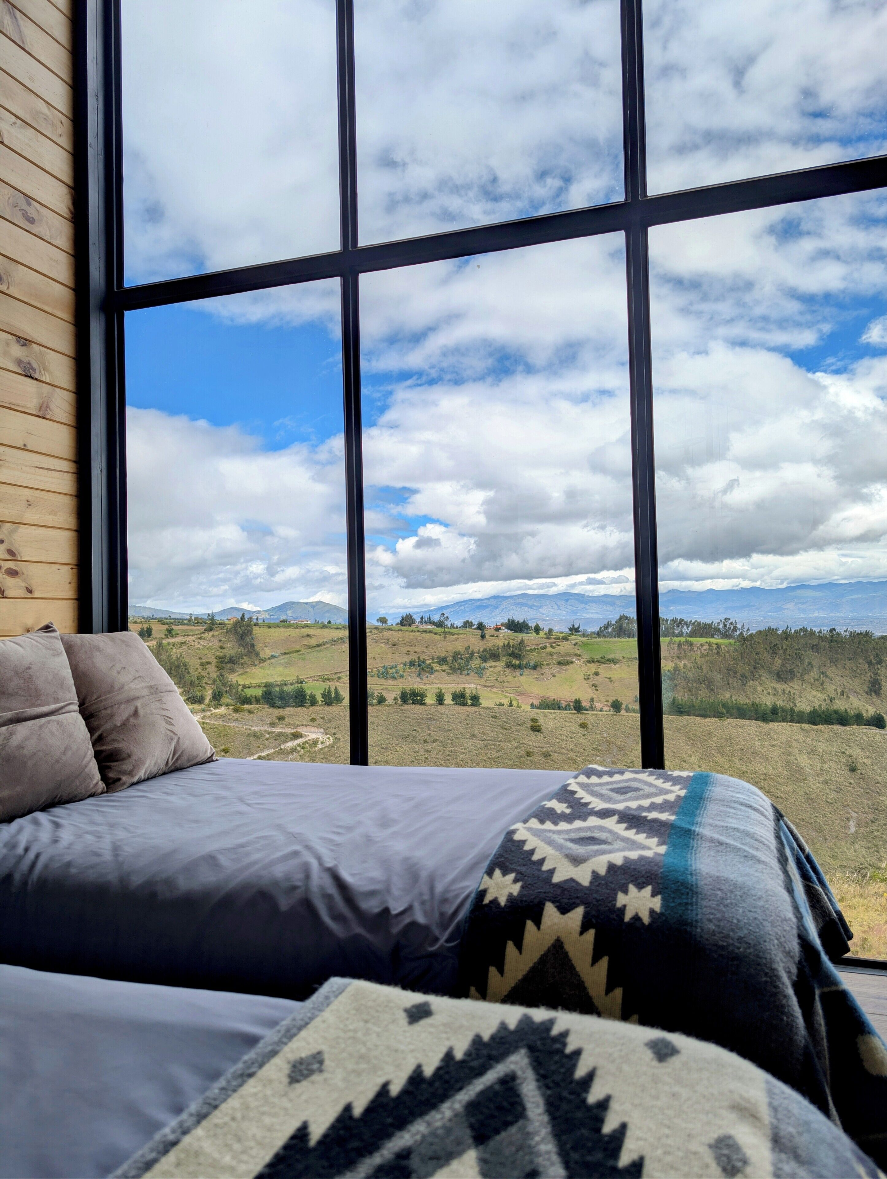 A bed with a view of a landscape through large windows.