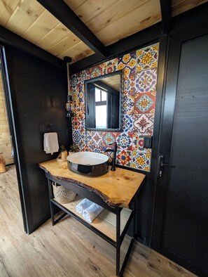 Un baño con tocador de madera, lavabo redondo, espejo y salpicadero de azulejos coloridos.