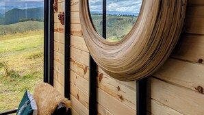 Espejo redondo sobre una pared de madera, con vista a un paisaje montañoso a través de una ventana.