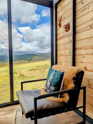 Una habitación con un ventanal grande, un sillón de cuero negro y un cojín verde, y paredes de madera.