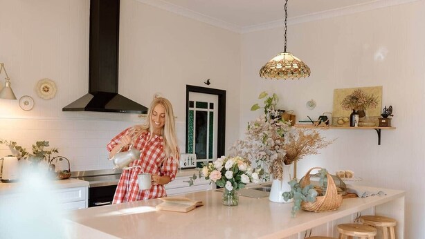 Cozinha com ilha central, banquetas, luminária pendente e objetos decorativos nas paredes.