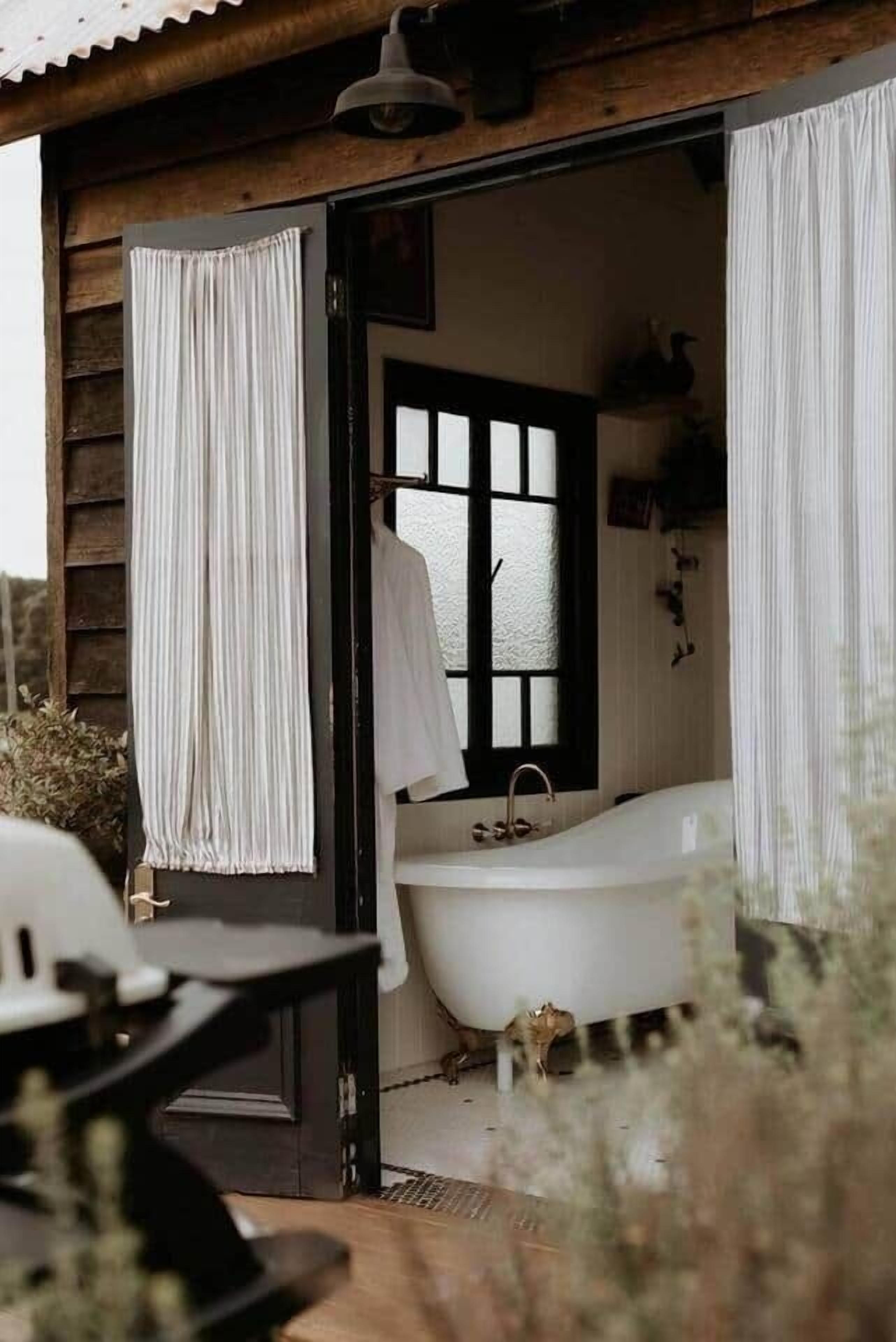 A rustic cabin with a wooden exterior, a white bathtub, and a window with black frames.