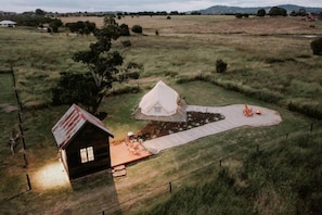 A rustic cabin with a small porch, a tent, and a fenced area with outdoor seating.